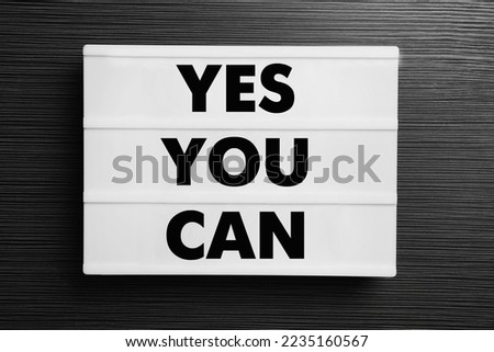 Lightbox with phrase Yes You Can on black wooden table, top view