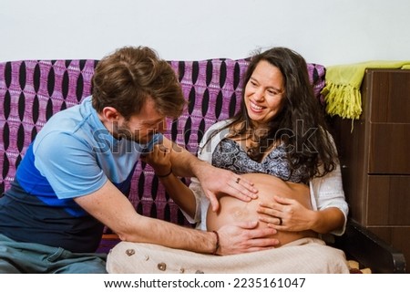 close-up of an adult man touching his wife's belly with both hands and watching their daughter move in her womb, sitting in the armchair, they are smiling, happily awaiting the birth of their baby. Royalty-Free Stock Photo #2235161047