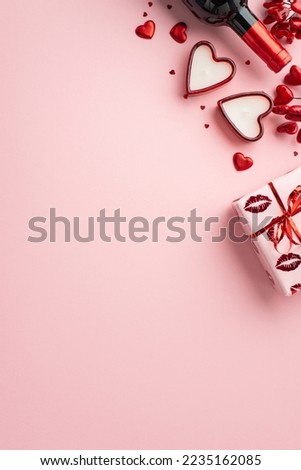 Saint Valentine's Day concept. Top view vertical photo of wine bottle giftbox heart shaped candles red hearts and confetti on isolated pastel pink background with copyspace