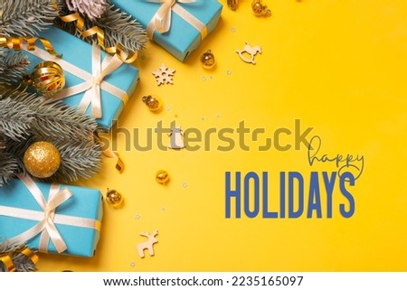 Happy Holidays text on yellow background with blue gifts, pine tree and festive decorations top view. Xmas greeting card.