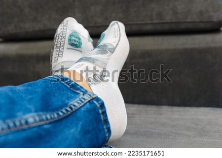 A man is in blue pants jeans lying in bed with an image of an American dollar on his sock.Indoors shot,selective focus.Closeup.