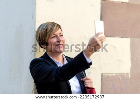 Smiling business woman standing outdoors while taking a selfie
