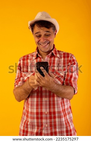Dark-haired man in a hat and colored shirt on an orange background with a mobile phone in different poses, calling, listening, touching or celebrating something he has seen on the screen