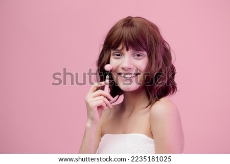  sweet, happy woman standing on a pink background with pink lighting from the side, with beautiful, styled hair, doing a facial massage with a pink roller. Horizontal photo with empty space