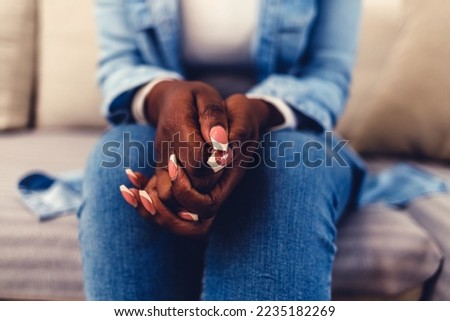 Close-up of clasped hands of an adult woman sitting on sofa, indoors. Concept of loneliness, stress, problem. Front view, selective focus on foreground