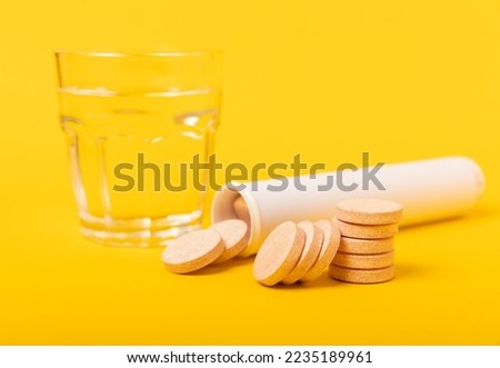 An effervescent vitamin tablet drops and dissolves in a glass of water on a yellow background. The concept of health. Medicine concept. Place for text.
