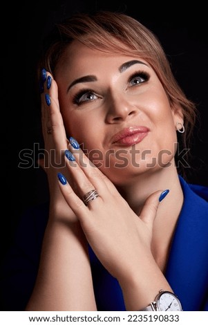 portrait of a beautiful caucasian woman in a blue jacket holds her hands near her face on a black background. High quality photo