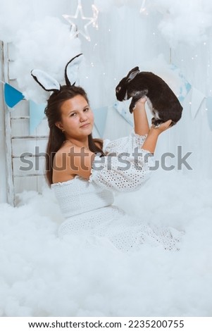 A girl with black bunny ears in the clouds is playing with a black rabbit. The relationship between a person and a pet