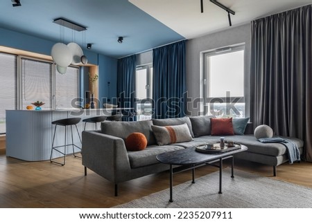 Creative composition of kitchen and living room interior with gray sofa, marble kitchen island, black coffee table, curtain, modern sculpture, gray rug and personal accessories. Home decor. Template.