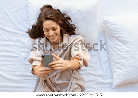 Photo of a happy 35 years old woman with smartphone in bed - she got a good news. View from the top.