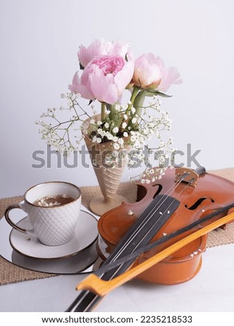 An artistic still life with a bouquet of pink peonies, a cup of tea and a violin. Vertical photo.