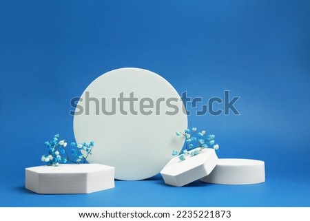 Product photography props. Podiums of different geometric shapes and flowers on blue background