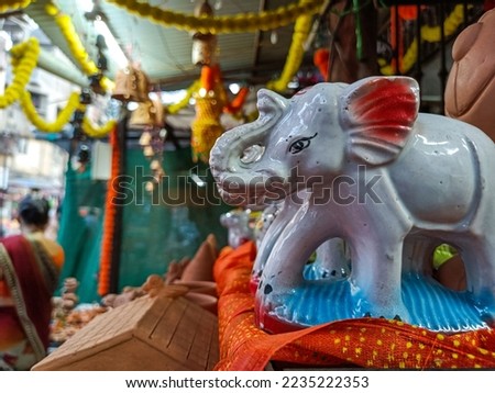 Stock photo of white color ceramic elephant statue or idol kept on wooden table for sale, other object, product and decorated shop on background.Picture captured under natural light at Kolhapur, India
