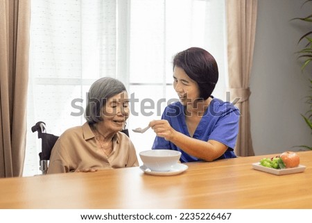 Caregiver feeding elderly asian woman with soup. Royalty-Free Stock Photo #2235226467