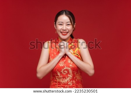 Young asian woman wearing qipao cheongsam dress make a wish on red background for Chinese new year festival Royalty-Free Stock Photo #2235230501