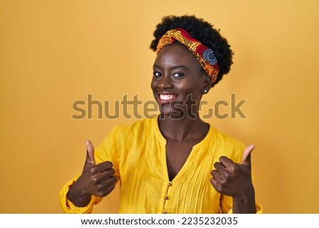 African young woman wearing african turban success sign doing positive gesture with hand, thumbs up smiling and happy. cheerful expression and winner gesture. 