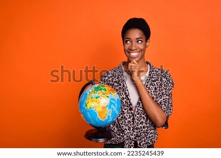 Portrait of attractive cheerful trendy minded girl holding globe deciding isolated over bright orange color background