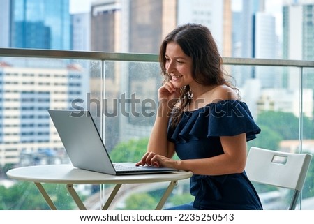 Business remotely. A girl works at her laptop on a balcony in the city center with a landscape view.