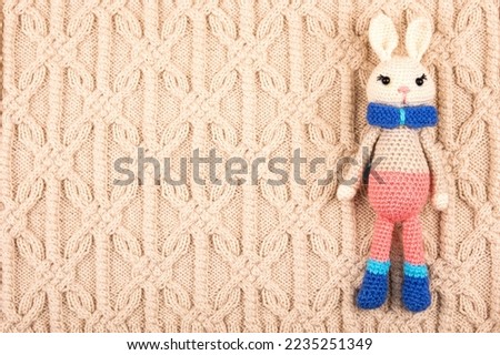 Knitted children's toy hare or rabbit on a knitted beige cloth. The symbol of 2023.