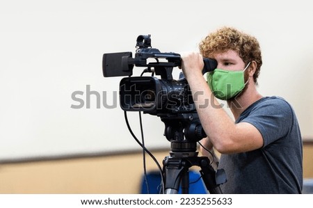 A young male Caucasian video operator with a green medical mask in the USA