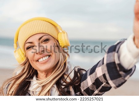 beautiful woman with headphones makes selfie on the background of a sea in vacation and travel, winter autumn hat color yellow