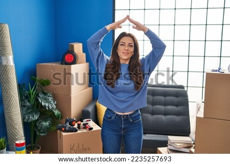 Young hispanic woman smiling confident doing house gesture with hands at new home