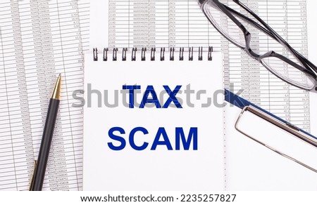 A white notepad with the text TAX SCAM a pen, reports and glasses lie on a white office table. View from above