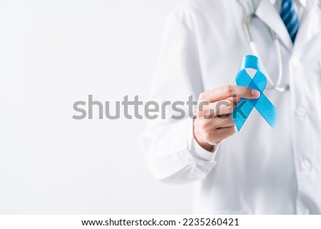 doctor in a white coat hands holding Blue ribbon for supporting people living and illness, Colon cancer, Colorectal cancer, Child Abuse awareness, world diabetes day, International Men's Day Royalty-Free Stock Photo #2235260421