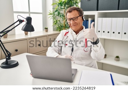 Senior doctor man working on online appointment doing happy thumbs up gesture with hand. approving expression looking at the camera showing success. 