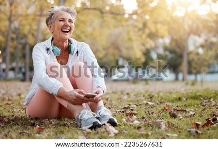 Health, nature and senior woman in park with phone and headphones to relax during fitness workout. Music, happiness and old lady laughing, sitting on ground in garden after running exercise in autumn Royalty-Free Stock Photo #2235267631