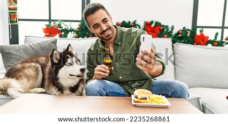 Young hispanic man make selfie sitting on sofa with dog by christmas decor at home