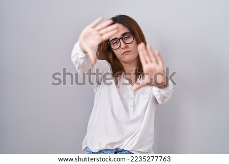 Brunette woman standing over white isolated background doing frame using hands palms and fingers, camera perspective 
