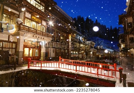 A cold snowy winter evening in Ginzan Onsen銀山温泉, which is a famous hot spring town in Obanazawa, Yamagata, Japan, with bridges spanning a stream flanked by historic buildings dating back to Taisho Era Royalty-Free Stock Photo #2235278045