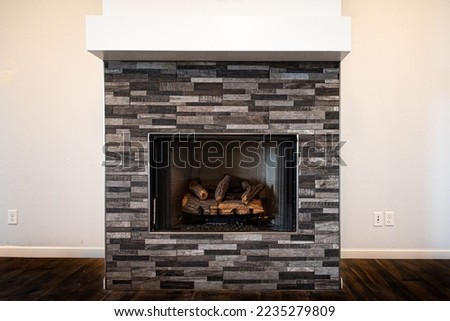 A gray fireplace with unlit firewood inside on a white background of living  room wall