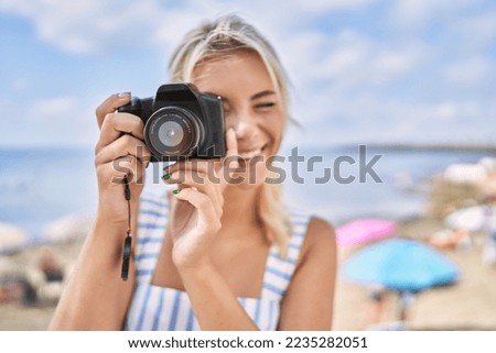 Young blonde girl smiling happy using camera at the beach.