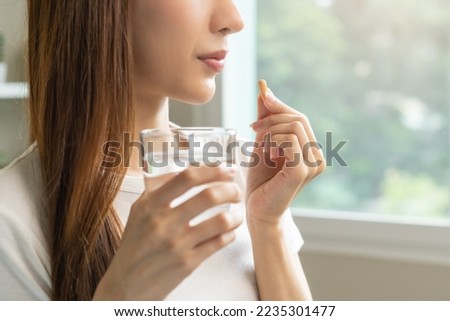 Dietary supplement, asian young woman, girl hand holding orange medical pill, take or eat vitamin C, D for treatment for skin, hair and nail strengthen with glass of pure water at home, healthcare. Royalty-Free Stock Photo #2235301477