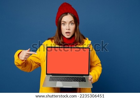 Young IT woman wear sweater red hat yellow raincoat outerwear work hold use laptop pc computer black screen isolated on plain dark royal navy blue background Outdoor wet fall weather season concept