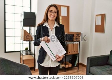 Young hispanic woman business worker holding paperwork standing at office