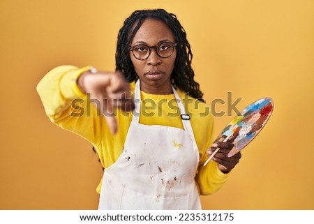 African woman holding painter palette looking unhappy and angry showing rejection and negative with thumbs down gesture. bad expression. 