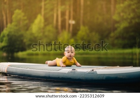 The child lies floating on the water on a large sup board. Water sports
