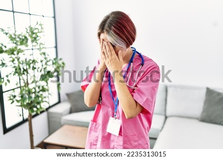 Young beautiful woman wearing doctor uniform and stethoscope with sad expression covering face with hands while crying. depression concept. 