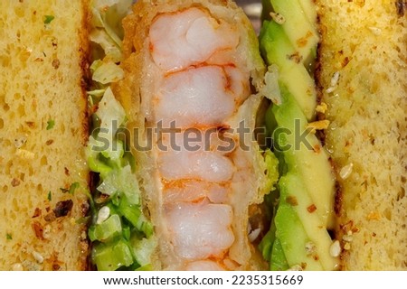 Cornbread sandwich with shrimp tempura, avocado and chukka seaweed. cucumber and sesame. Sandwich on a dark ceramic plate on a gray background with bronze inserts.