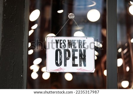 Inscription Yes we're open metal plate with black and white sign on glass door store, cafe, beautystore, barbershop after coronavirus lockdown quarantine. business reopen again.