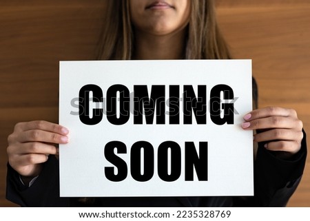 Coming soon. Woman holds a white page with orange text. Information sign, opening event, business and premiere event.