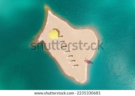 Woman sunbathes on the one of a lot of deck chair with umbrella and sup board on a small uninhabited, desert sand island  in the middle of sea. Drone view, aerial view, top view