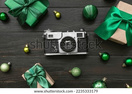 Photo camera with Christmas balls and gifts on black wooden background