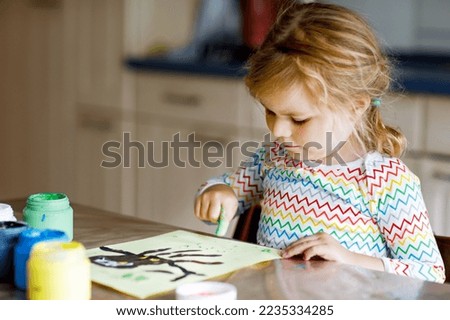 Little creative toddler girl painting with finger colors an owl bird. Active child having fun with drawing at home, in kindergaten or preschool. Games, education and distance learning for kids