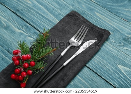 Napkin with cutlery and fir branch on color wooden background, closeup