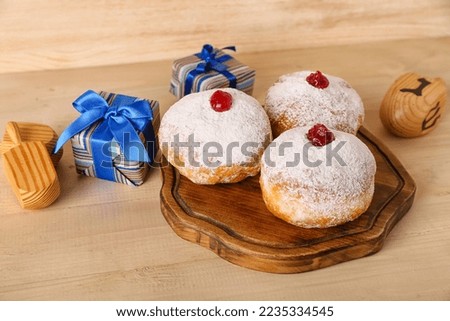 Board with tasty donuts, gifts and dreidels for Hannukah celebration on wooden background