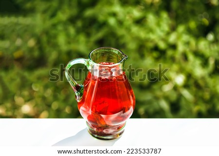 Green jar of cranberry lemonade outdoor. Shallow depth of field. Green bokeh in background. Focused on upper part of jar